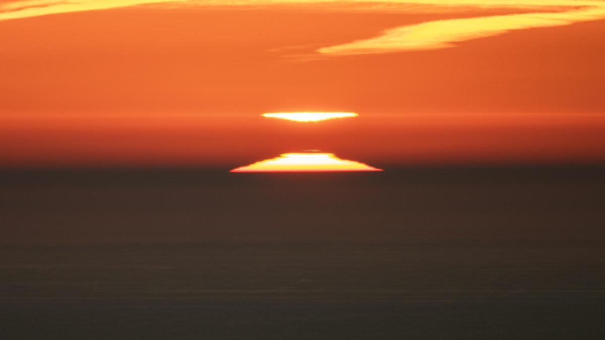 Salida del Sol en Barcelona, el 26 de enero, con inversión térmica. A medida que el Sol sube distorsionado por capas de diferente temperatura su imagen invertida baja desde el nivel de inversión, se tocan, se cruzan y luego el Sol supera ese nivel y su imagen desciende distorsionada. En esta imagen puede apreciarse un poco el rayo verde