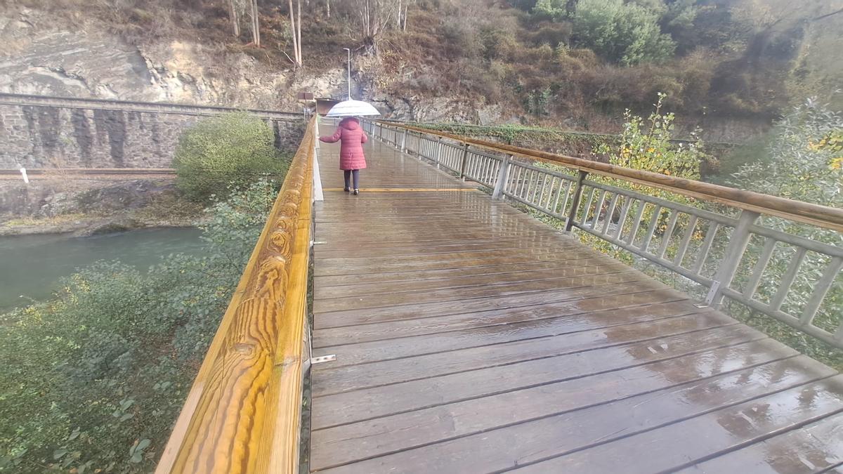 Una vecina transita por el centenario puente de Bustiello apoyada en en la barandilla que acaba de ser arreglada.