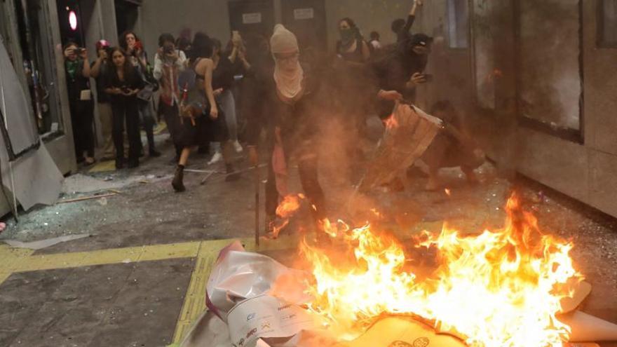 Manifestantes rompen cristales y queman papeles en un edificio.