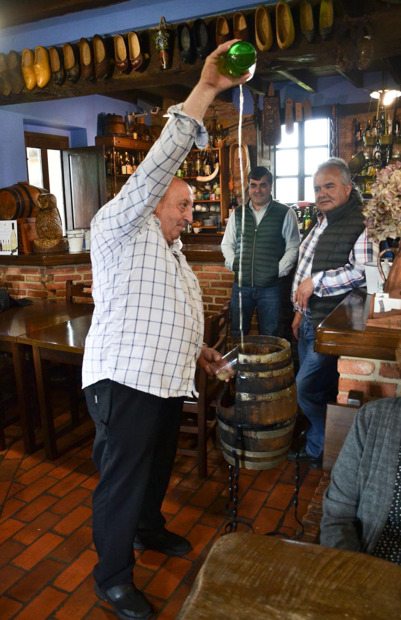 Rafael Peón escanciaun culete de sidra en presencia de Nino Fernández y Antonio Arias en el chigre restaurante Uncal en Güexes (Parres). 