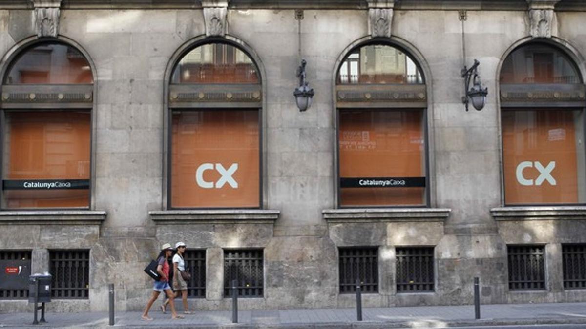 Dos personas pasan delante las oficinas centrales de CatalunyaCaixa, en la Via Laietana de Barcelona.