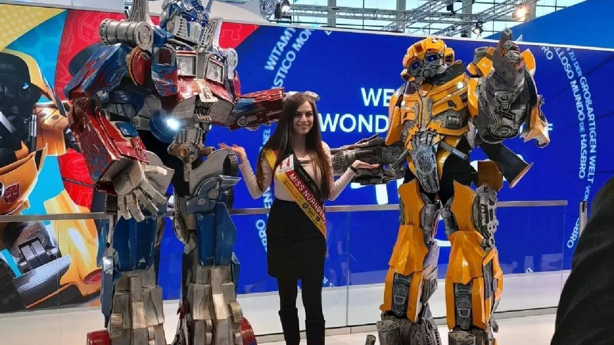 Dos miembros de Cosplay Vinaròs posan con sus espectaculares disfraces de Transformers junto a Miss Núremberg en el estand de Hasbro en la Feria Internacional del Juguete que acoge la ciudad alemana.