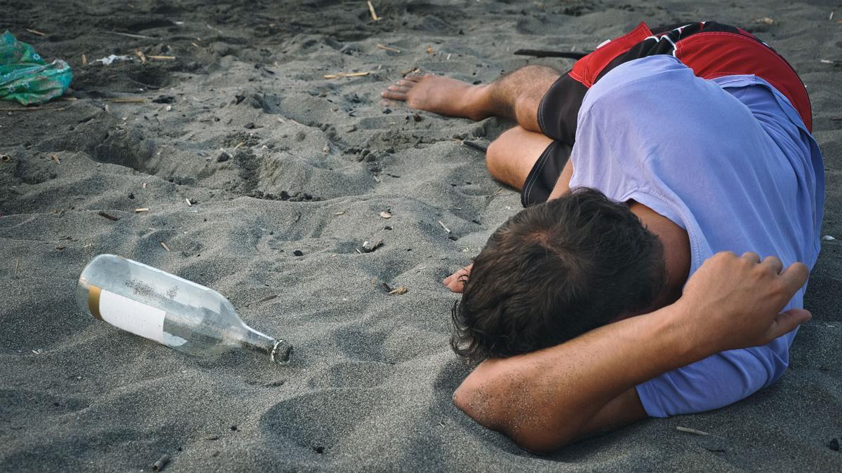 Un joven duerme en una playa tras una noche de botellón.