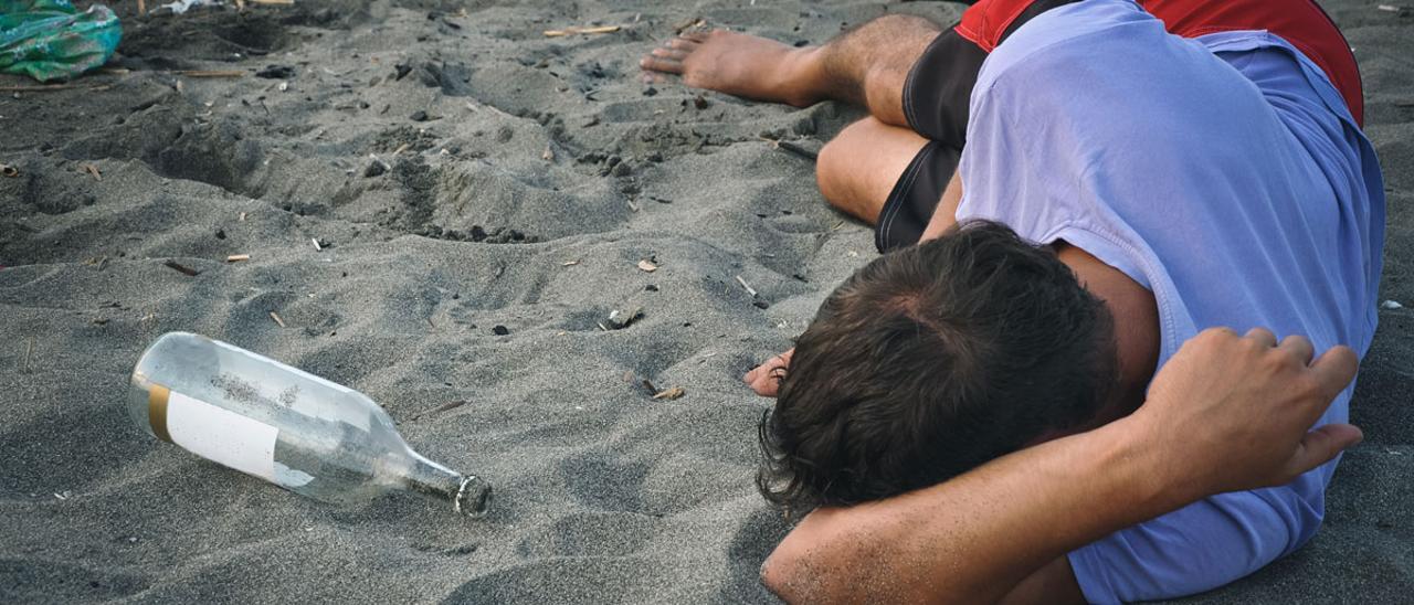 Un joven duerme en una playa tras una noche de botellón.
