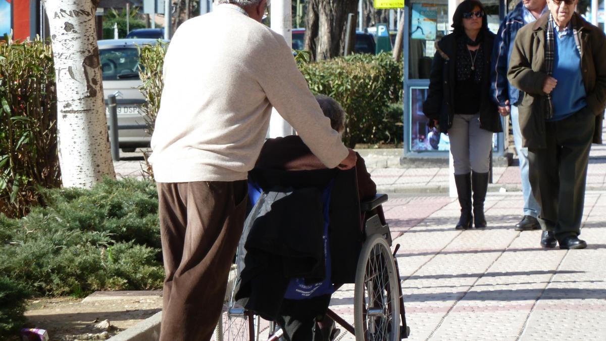 Un hombre pasea a una mujer dependiente en silla de ruedas.