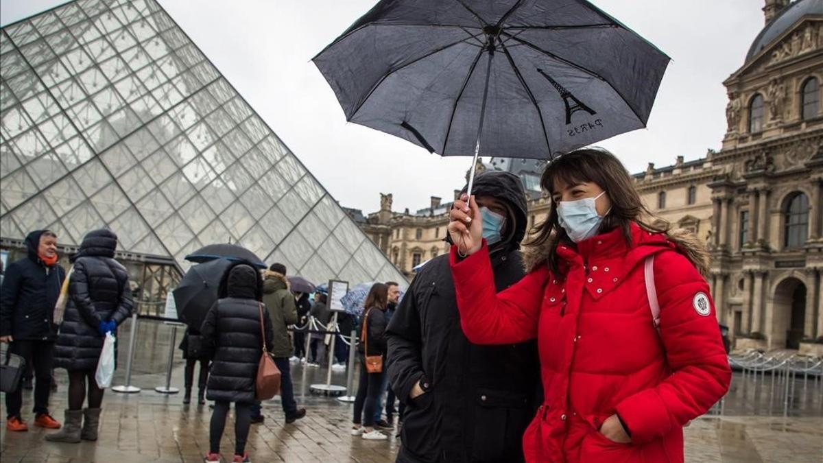 Turistas con mascarillas para protegerse del coronavirus, frente al Louvre de París