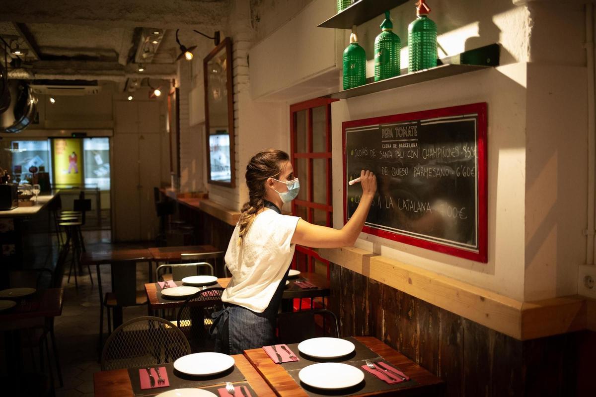 Una camarera apunta platos en una pizarra de un bar en Barcelona.