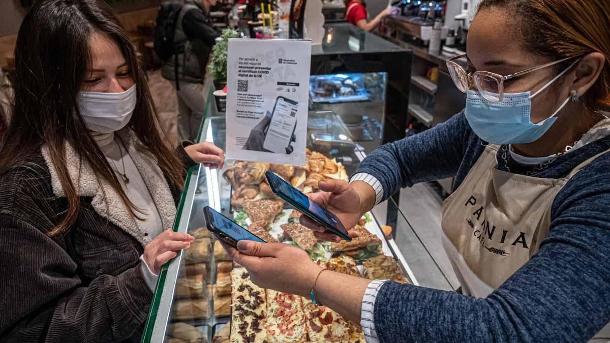 Una dependienta de una panadería de Barcelona comprueba el pasaporte covid de una clienta