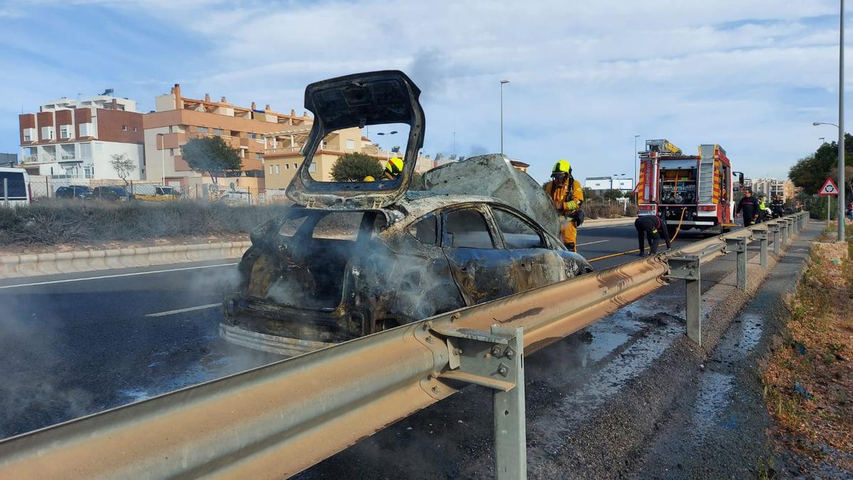 Los bomberos en la intervención para sofocar el fuego en el coche, que ha quedado prácticamente calcinado