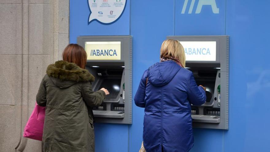 Dos señoras retiran dinero en los cajeros de una oficina de Abanca.