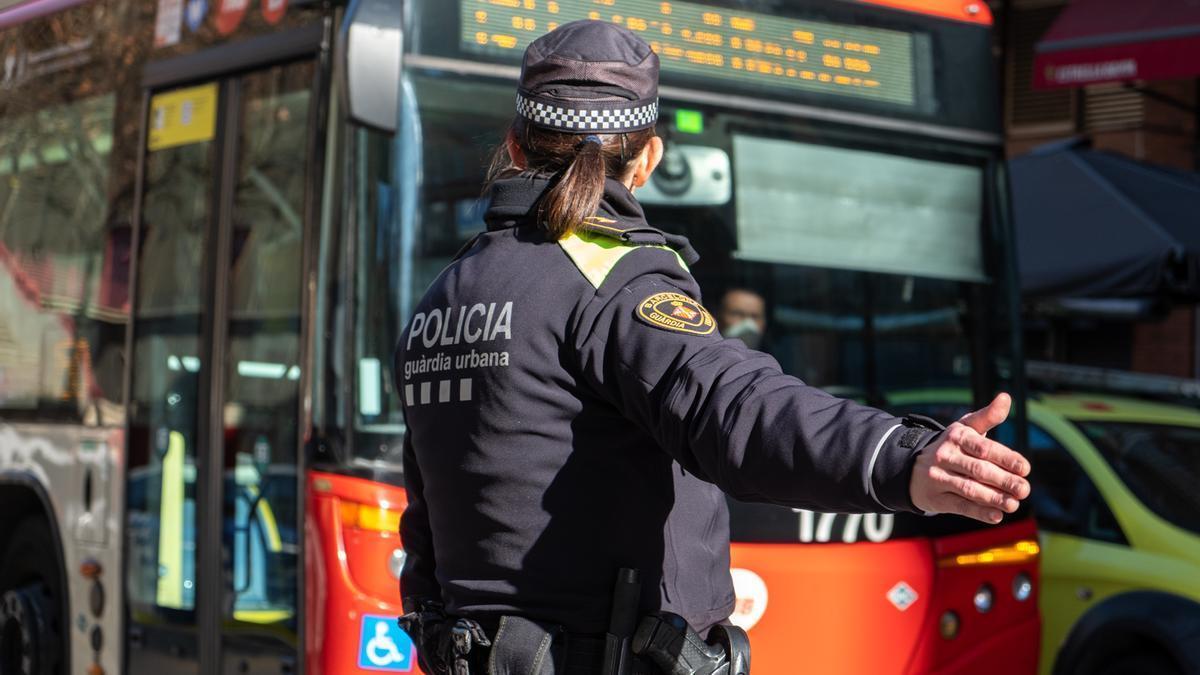 Imagen de una agente de la Guardia Urbana frente a un autobús.
