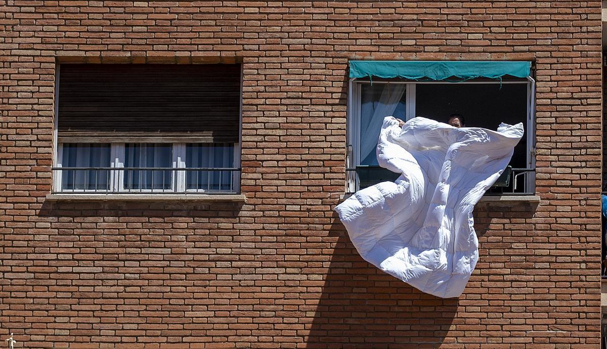 Una mujer sacudiendo un edredón desde la ventana.