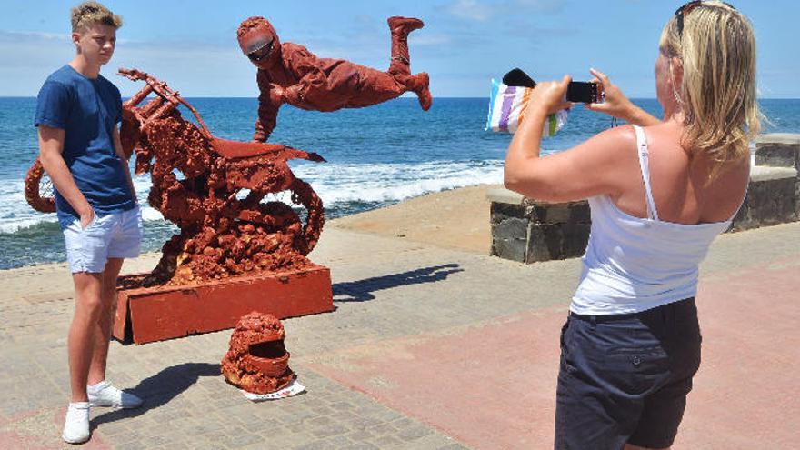 Turistas fotografiándose en el Paseo de Meloneras con la escultura humana de un motorista por los aires de fondo.