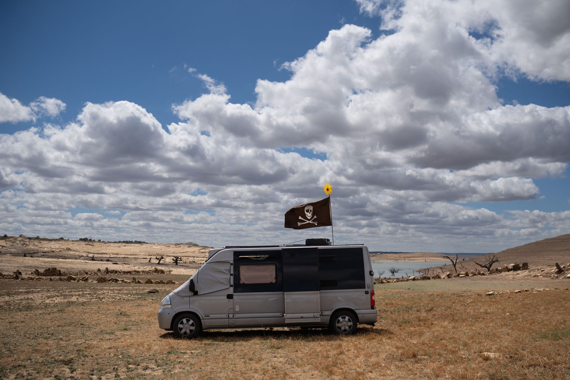 Una furgoneta camperizada con una bandera pirata junto al embalse de Almendra.