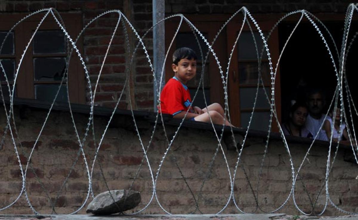 Un nen observa a través del filat que protegeix la tomba d’un màrtir musulmà Srinagar, regió de Caixmir, Índia.