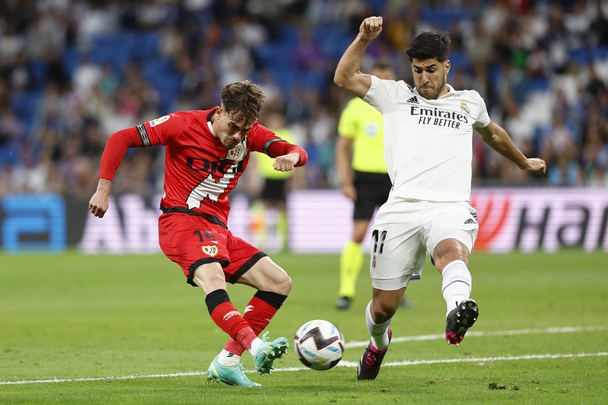 MADRID, 24/05/2023.- El defensa del Rayo Vallecano, Pep Chavarría (i), golpea el balón ante el centrocampista del Real Madrid, Marco Asensio, durante el encuentro correspondiente a la jornada 36 de primera división que han disputado hoy miércoles en el estadio Santiago Bernabéu, en Madrid. EFE / Rodrigo Jiménez.