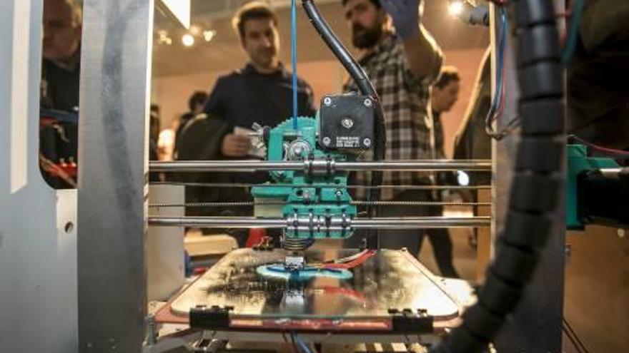 Dos jóvenes observan el funcionamiento de una impresora 3D.