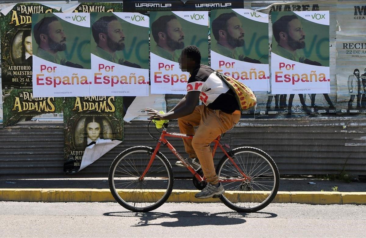 Un joven en bicicleta pasa junto a una pared llena de carteles de Vox en una calle de El Ejido (Almería) que dio una sorpresa relativa en las pasadas elecciones andaluzas al convertirse en el primero de España en el que esta formación política era la fuerza más votada, sobrepasando al PP.