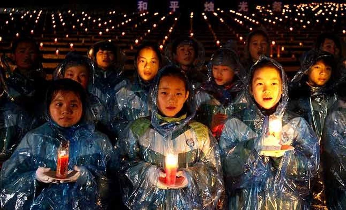 Alumnes amb impermeables porten espelmes durant una cerimònia per commemorar el 73 aniversari de la massacre de Nanjing, al Museu de la Massacre de Nanjing a Nanjing (Xina).
