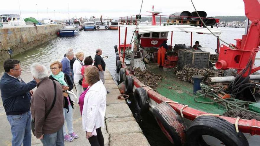 Los turistas observan cómo se limpia la ostra en la cubierta de un barco amarrado al puerto. // Muñiz