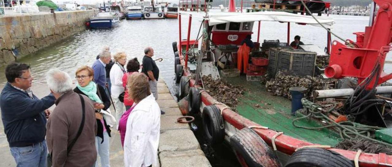 Los turistas observan cómo se limpia la ostra en la cubierta de un barco amarrado al puerto. // Muñiz