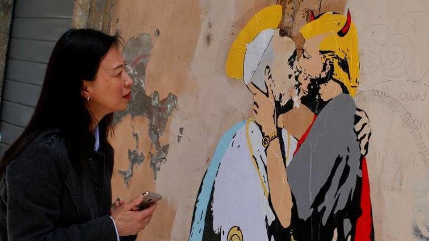 Una mujer observa en Roma un mural que representa a un diabólico Trump besando en los labios al Papa. // Reuters