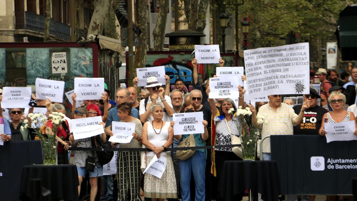 Persones amb cartells protestant a l&#039;acte de commemoració dels cinc anys dels atemptats del 17 d&#039;agost per la investigació que s&#039;ha fet del 17-A, a la Rambla de Barcelona.