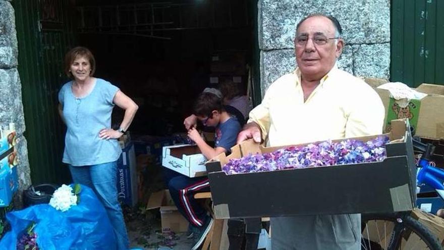 Antonia Piñeiro, al fondo, con el vecino Andrés Alves, que ayuda con las cajas de flores.