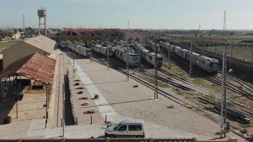 Playa de vías llenas de trenes con los antiguos talleres de FGV, al fondo.