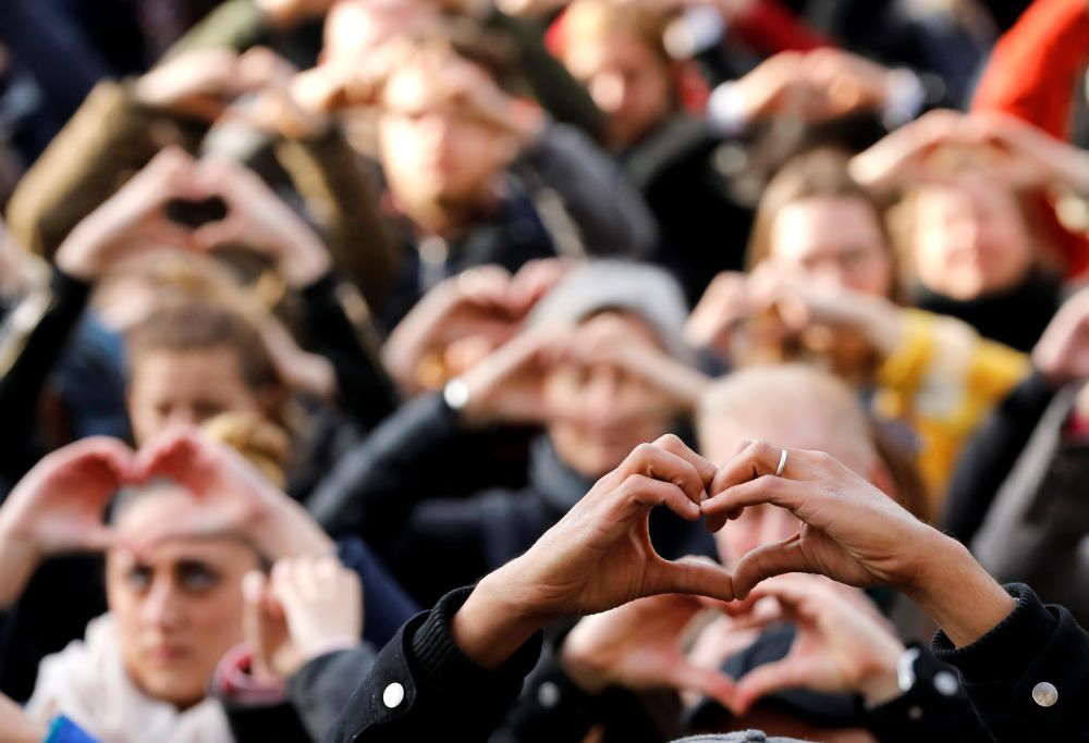 Asistentes a la concentración por el primer aniversario de los atentados de Bruselas forman corazones con sus dedos ante el edifico de la Bolsa.