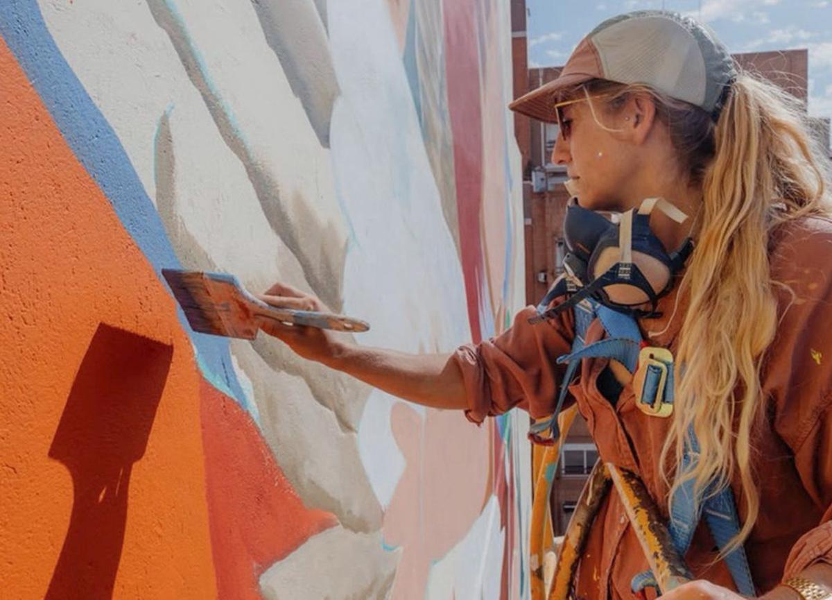 D’esquerra a dreta, un mural de Lula Goce, Julieta XLF pintant una peça, la persiana de La Costelera i la persiana de la Vermuteria D’Clot, totes dues pintades per Roc Blackblock. | LULA GOCE
