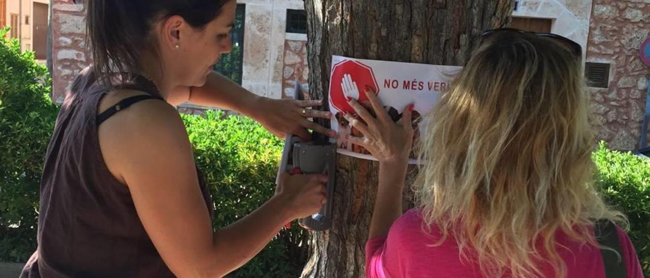 Arriba, dos mujeres cuelgan carteles de la concentración del domingo.