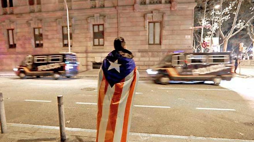 Un hombre con una ´estelada´ a la espalda observa dos furgones de la Policía Nacional en la zona del Parlament catalán.