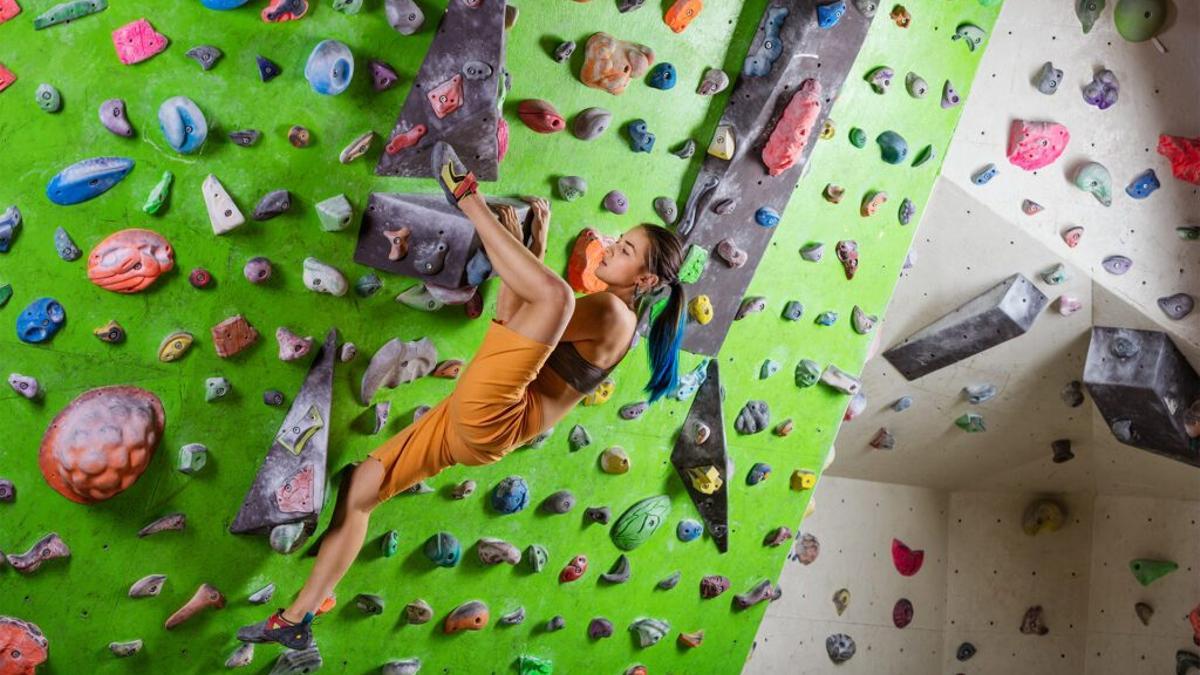 Una joven practica escalada en un rocódromo indoor.