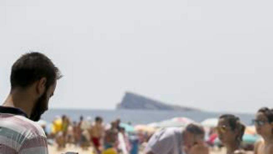 Un joven consulta su móvil en la playa de Benidorm.