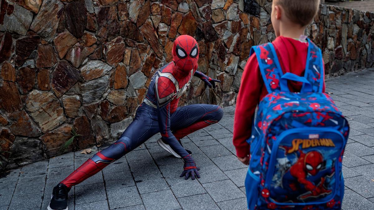 Un niño con mochila de Spiderman mira al hombre araña de Santa Coloma. 