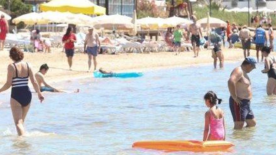 Varias personas pasean y se bañan junto a la torre del socorrista.