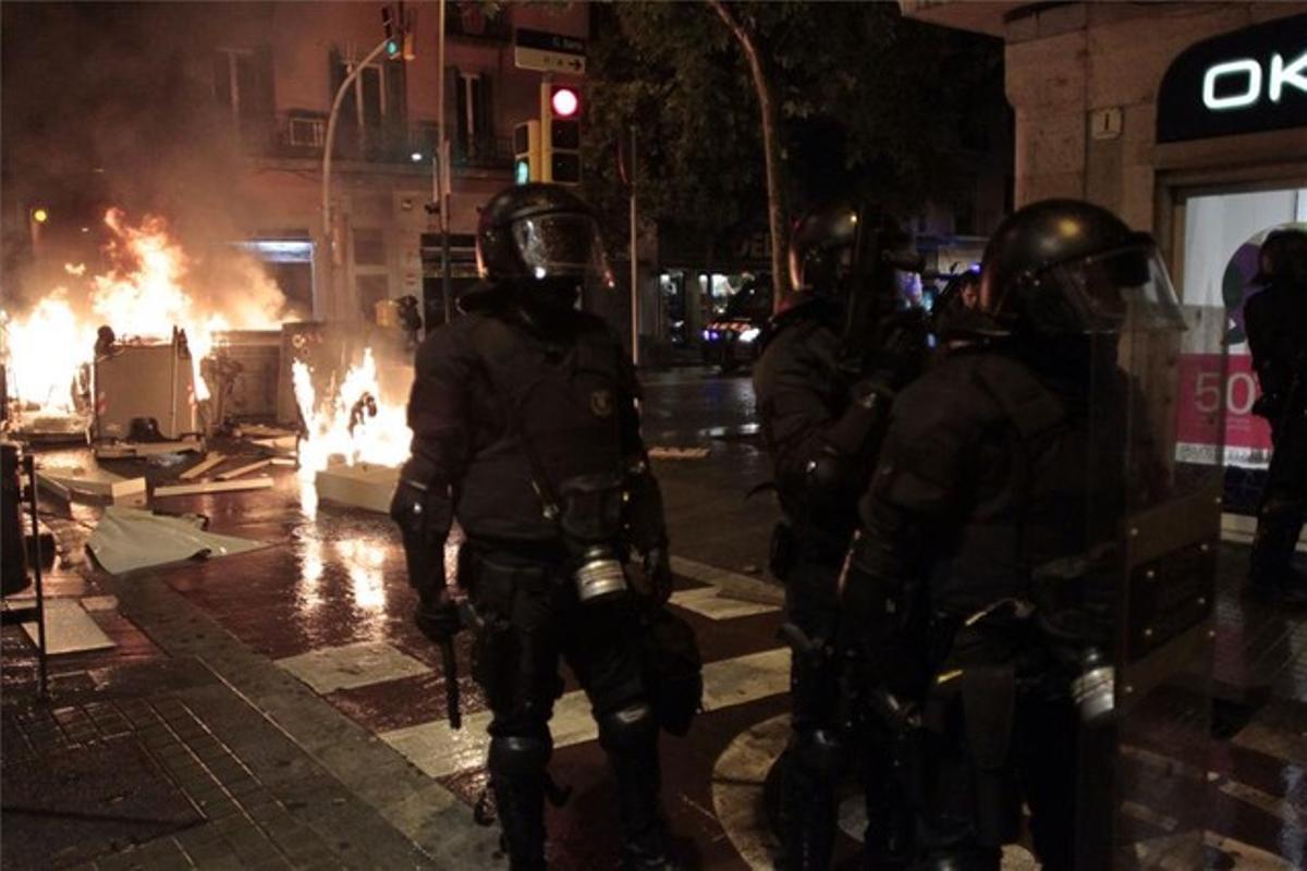 Agentes de policía vigilan en una calle de Sants mientras arde mobiliario urbano durante las protestas por el desalojo de Can Vies.