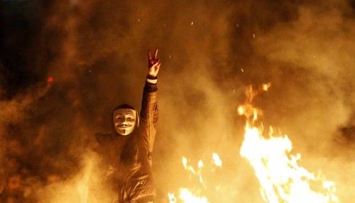 An anti-government protester wearing a Guy Fawkes mask gestures behind a barricade that they set on fire during a demonstration in Ankara