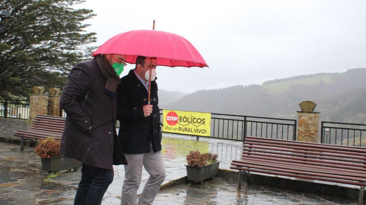 El alcalde santallés, Víctor Lorido, cobija a Barbón de la lluvia mientras pasan junto a una pancarta contra los eólicos. | T. Cascudo