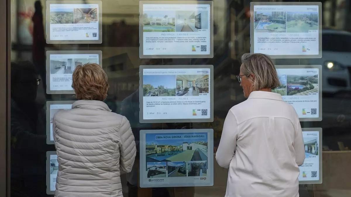Dos mujeres frente al escaparate de una inmobiliaria en Girona.