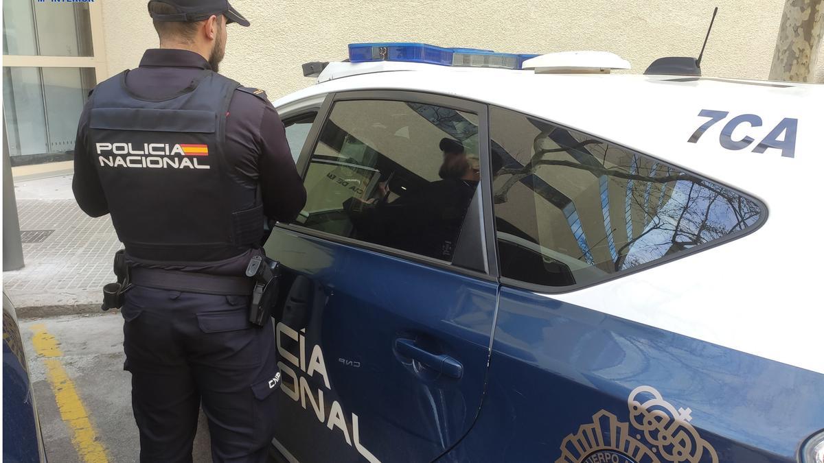 Agente de la Policía Nacional de espaldas, junto a un coche patrulla.