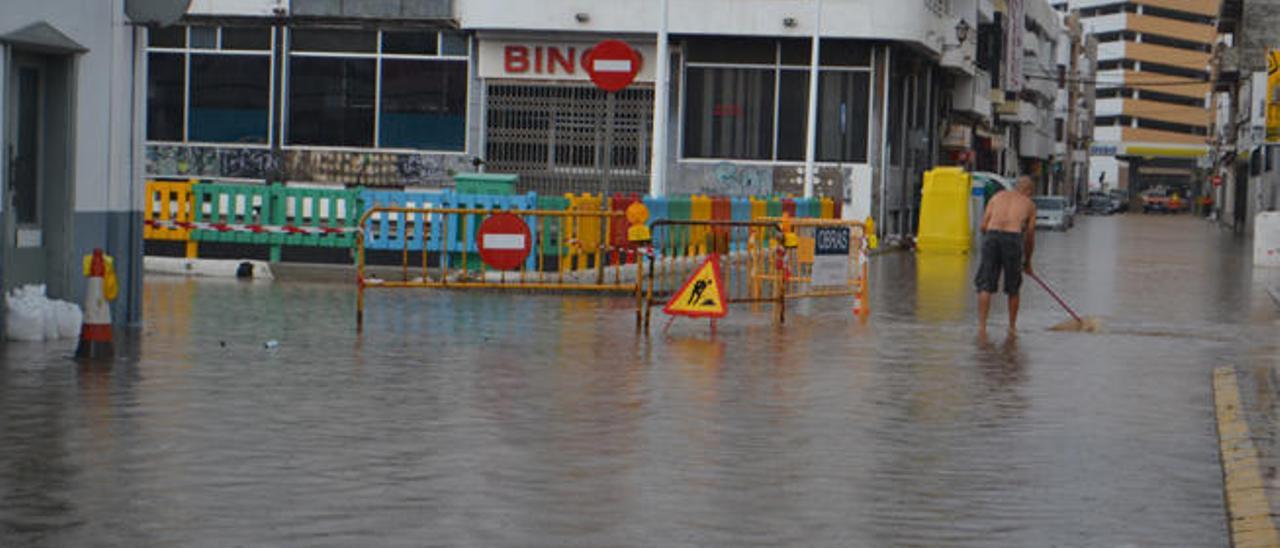 El vecino de Arrecife Nicolás Martín en la calle Portugal totalmente anegada tratando de achicar agua junto a una alcantarilla.