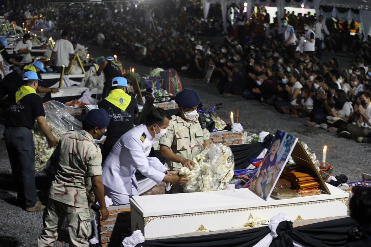  Funcionarios tailandeses depositan flores de sándalo sobre los ataúdes de las víctimas del tiroteo masivo en las piras funerarias 