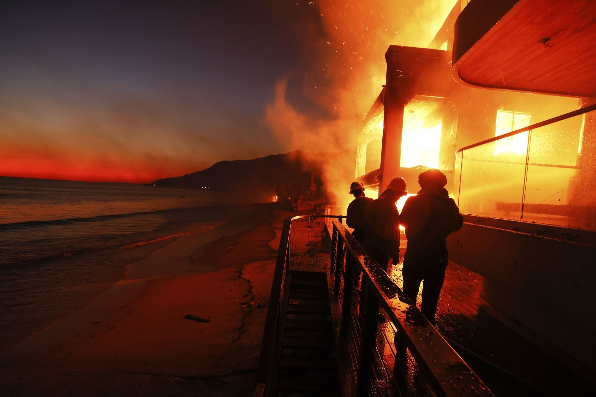 Firefighters work from a deck as the Palisades Fire burns a beachfront property Wednesday, Jan. 8, 2025, in Malibu, Calif. (AP Photo/Etienne Laurent) Associated Press / LaPresse Only italy and Spain. EDITORIAL USE ONLY/ONLY ITALY AND SPAIN