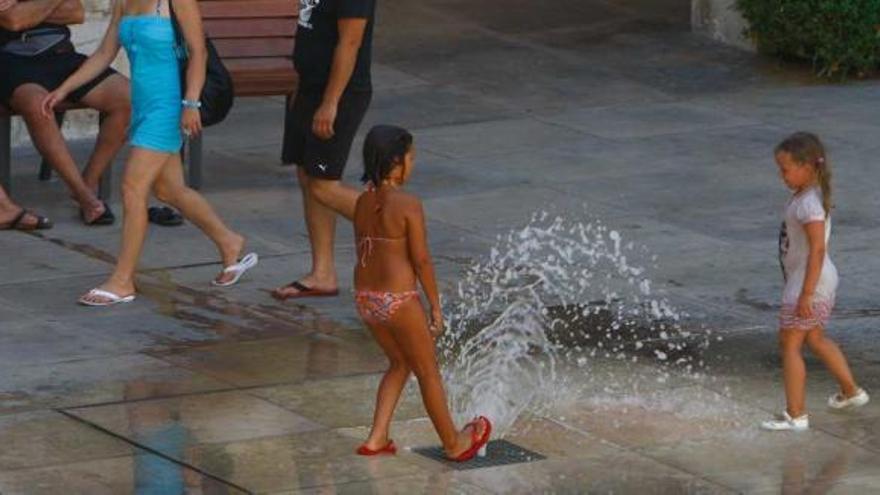 Dos niñas juegan en la fuente de la plaza del Ayuntamiento para mitigar el calor.