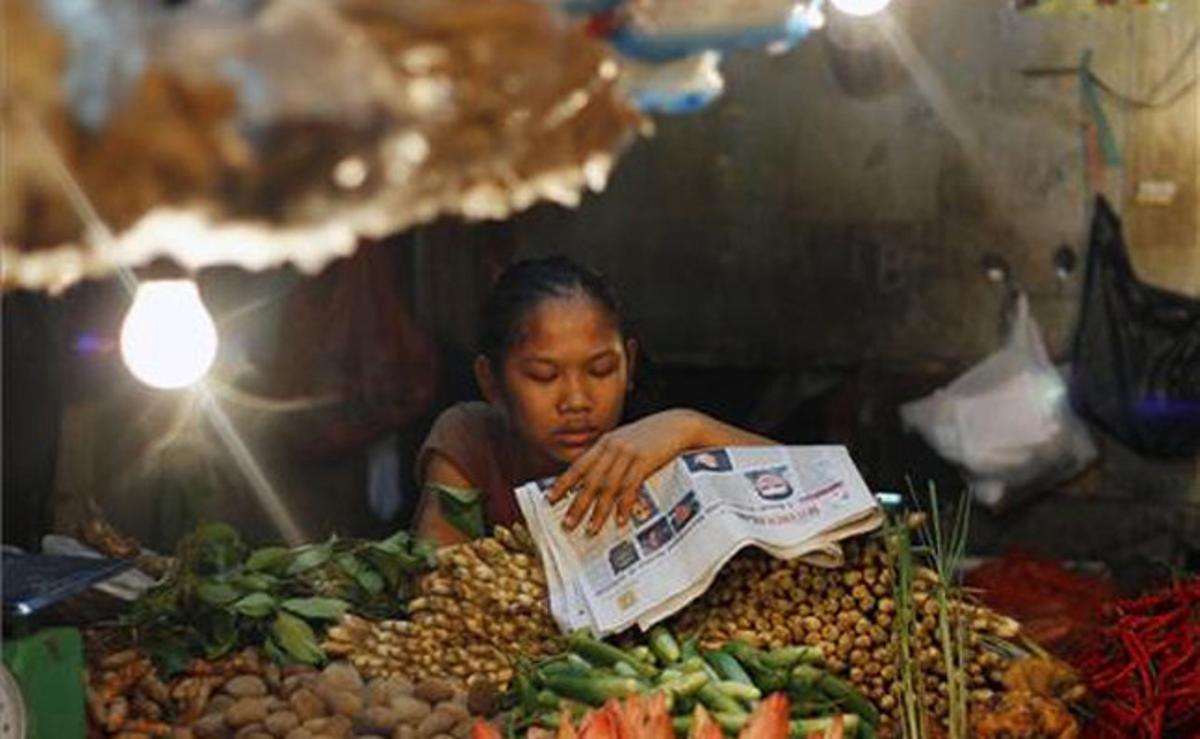 Una venedora de verdures llegeix el diari mentre espera clients en un mercat de Jakarta (Indonèsia).