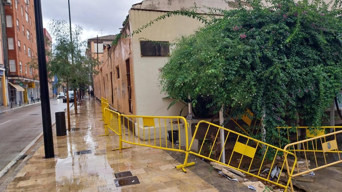 La calle Alzira de Gandia, con la valla que acota la acera junto a las naves en ruina.