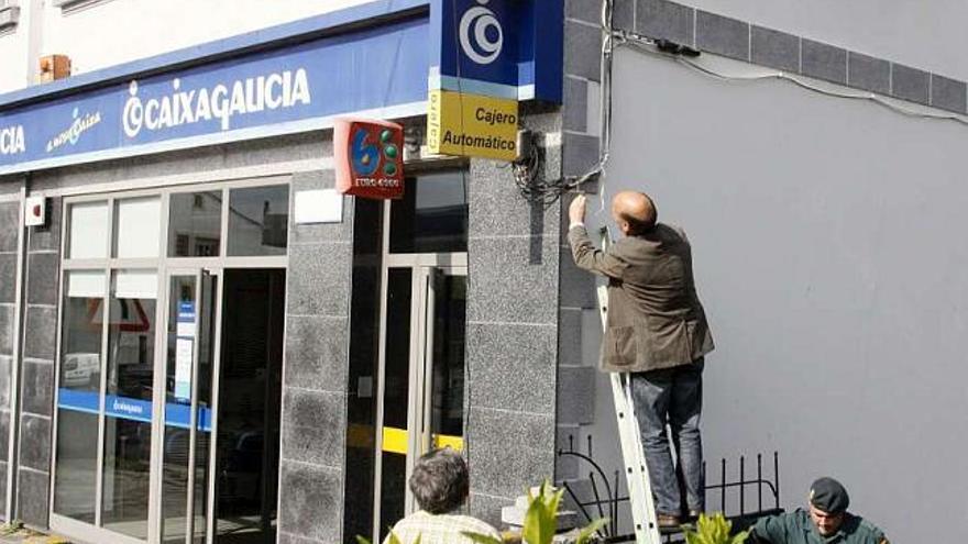 Agentes de la Guardia Civil inspeccionan la fachada de la sucursal de Caixa Galicia en Guntín. / eliseo trigo