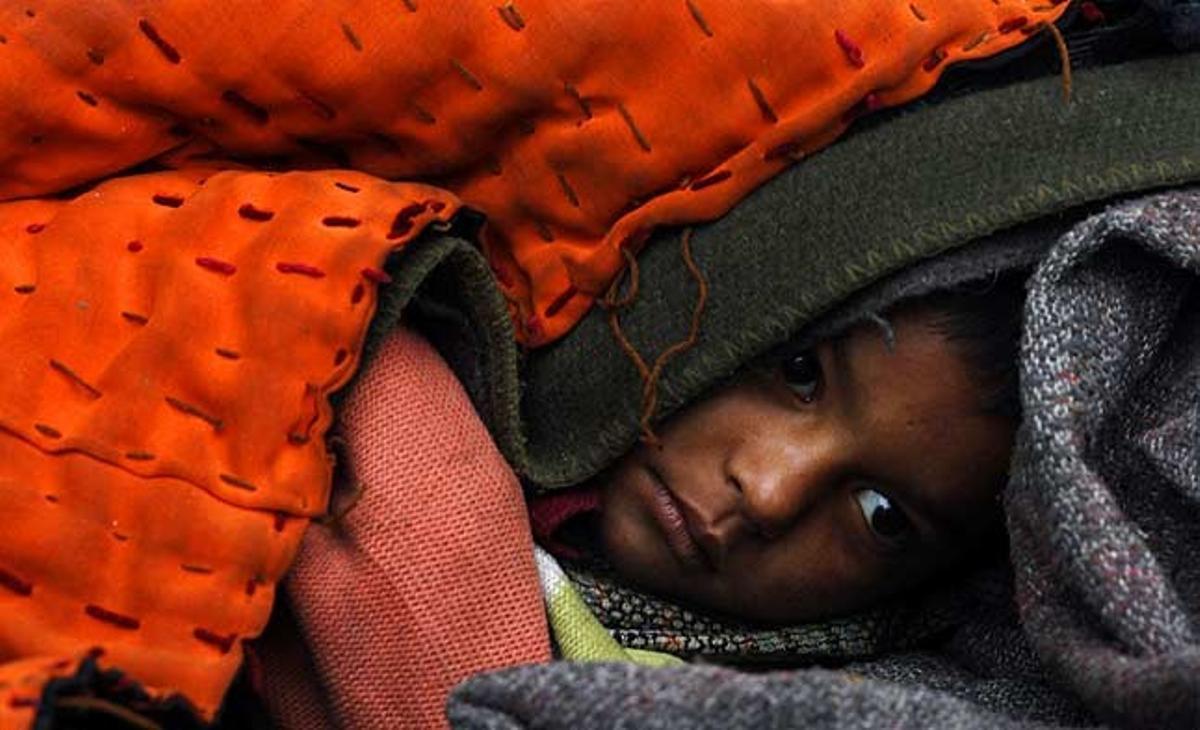 Un nen sense llar es tapa amb diverses mantes en un matí fred a Allahabad (Índia).